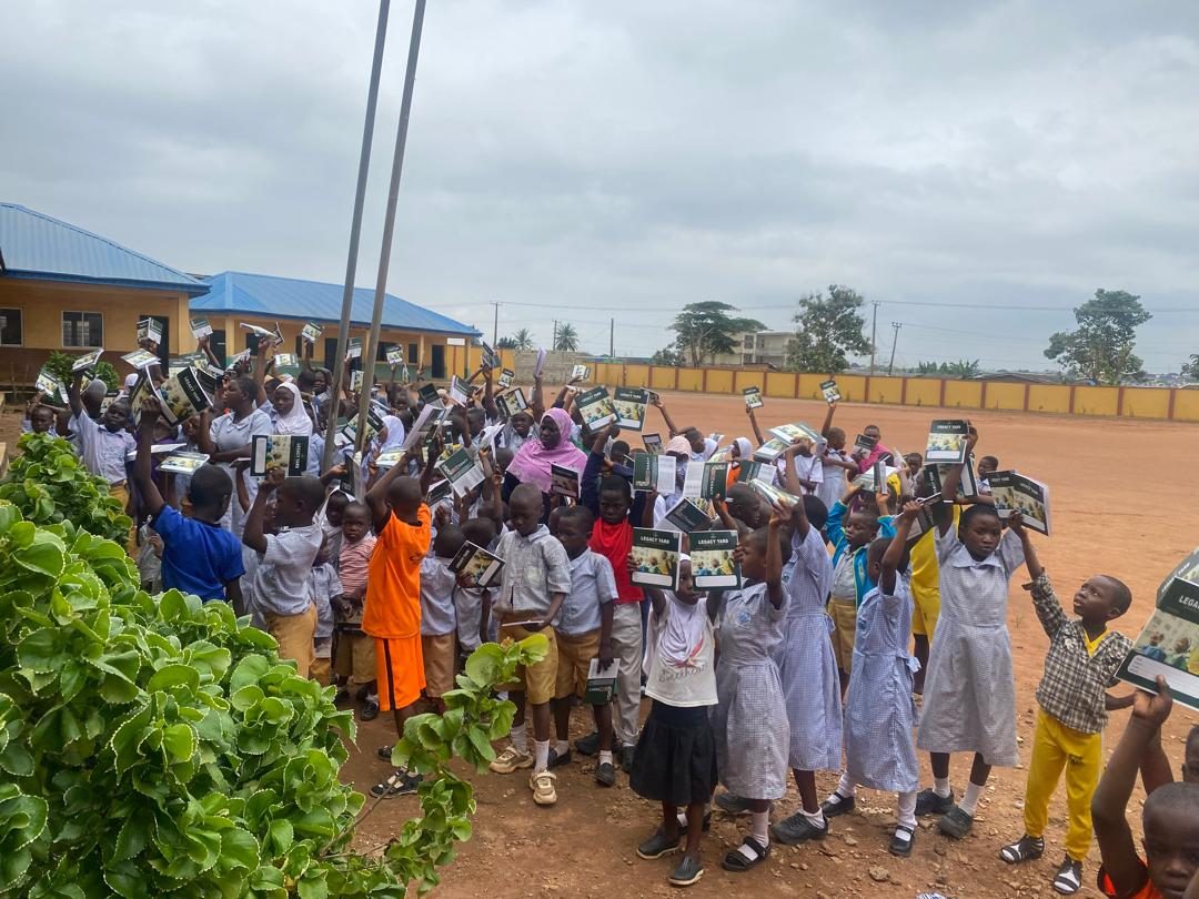 School pupils holding up Legacy Yard exercise books in a school compound