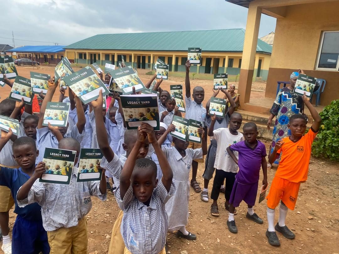 Children holding up Legacy Yard exercise books outside their school building
